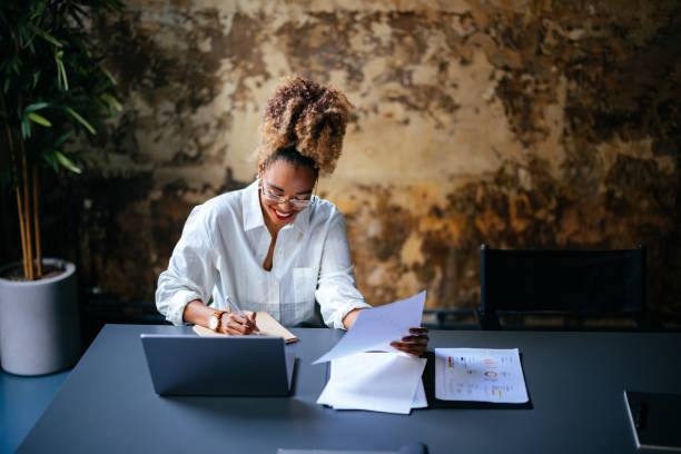 istock Smiling Businesswoman Using A Laptop Computer And Writing Report In Notebook  In The Cafe 1456192709