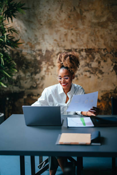 istock Smiling Businesswoman Holding Document While Using A Laptop Computer In The Cafe 1456192723