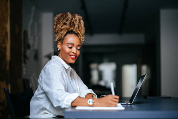 istock Happy Businesswoman Using A Laptop Computer And Writing Notes In Notebook In The Cafe 1456193004