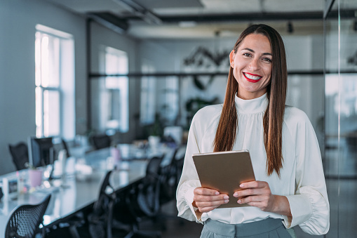 Shot of successful young businesswoman standing in the office and holding digital tablet. Portrait of a beautiful smiling businesswoman standing in her office and looking at camera.