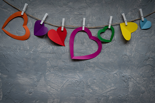 Multi colored hearts on rope with clothespins, on a grey background