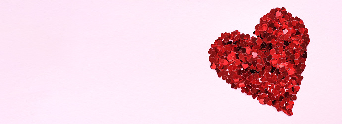 Background for Valentine's Day or a wedding. A heart of shiny red little decorative hearts on a pink background. Flat design, space for text.