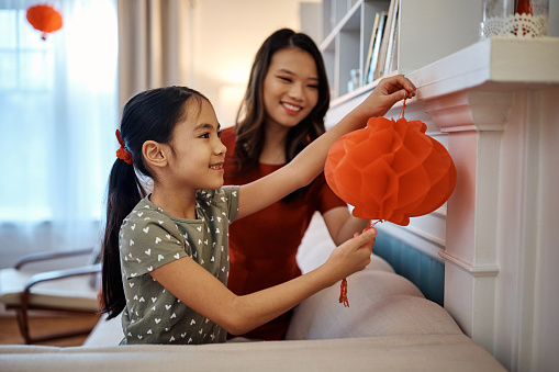 Happy Asian girl hanging lantern with her mother while decorating home for Chinese New Year.