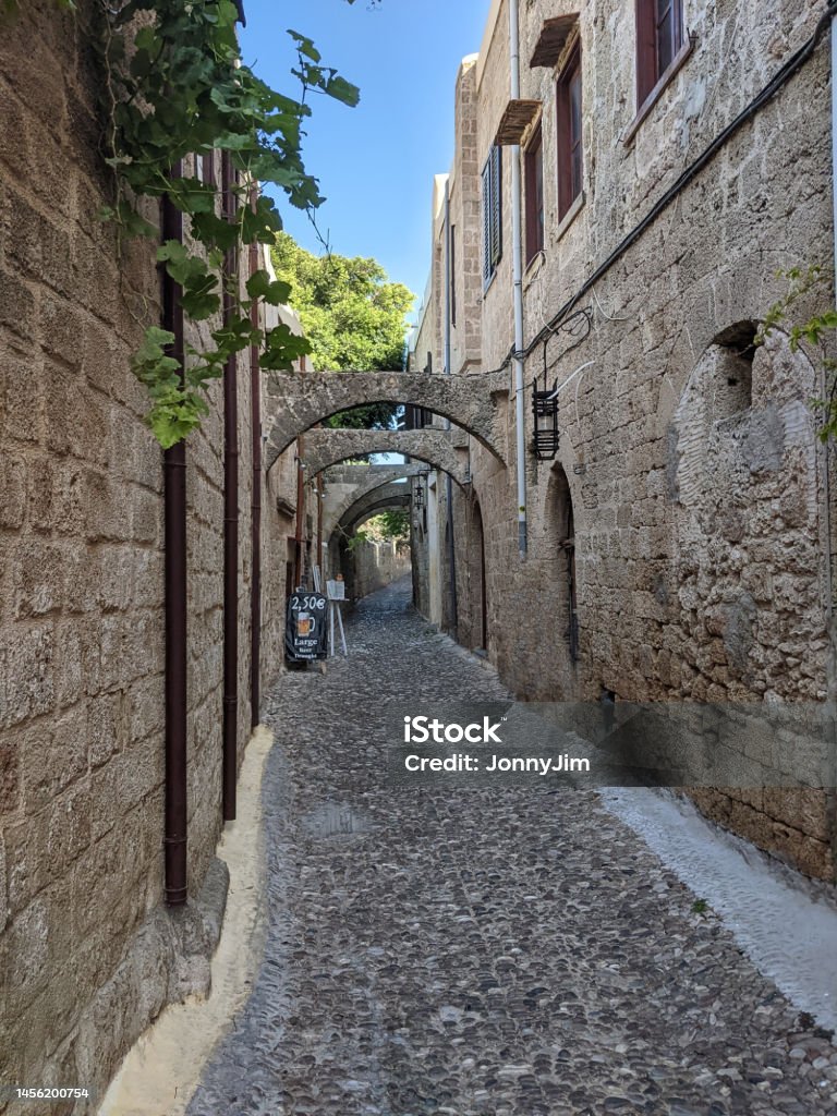 Backstreet in Rhodes town, Rhodes, Greek island A cobblestone backstreet with high stone walls of old buildings in the capital of the Greek island of Rhodes Alley Stock Photo