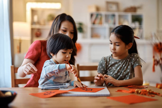 Chinese kids learning to write Fai Chun with their mother while decorating home for Lunar New Year. Asian boy writing calligraphy with mother and sister while preparing for Chinese New year celebration at home. family word art stock pictures, royalty-free photos & images