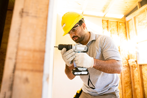 Construction worker installing drywall in unfinished wooden house
