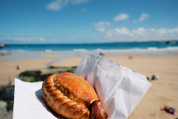 POV of a hand holding a Cornish Pasty at Towan Beach, Newquay, Cornwall on a bright sunny June day. stock photo