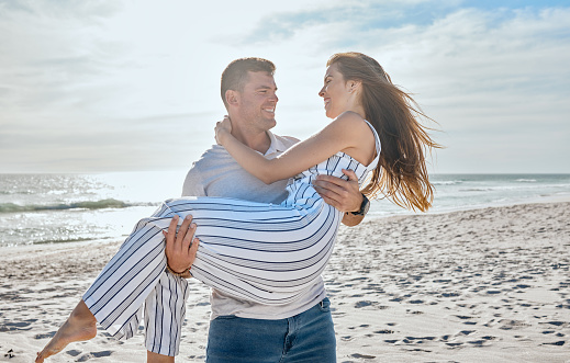 Couple, love and carrying at beach, holiday and freedom on anniversary, romance and travel together in Hawaii. Man, woman and happy vacation, smile and support in marriage relationship at the ocean