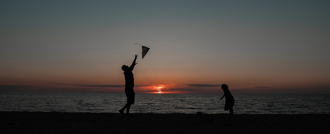 happy family father and child daughter run with kite in the meadow. silhouettes on the background of the sea sunset. High quality photo.