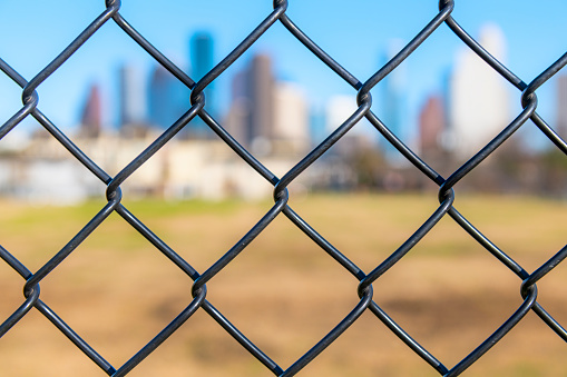 Both modern and historic buildings of downtown Houston, Texas blurred behind a chainlink fence in the foreground.