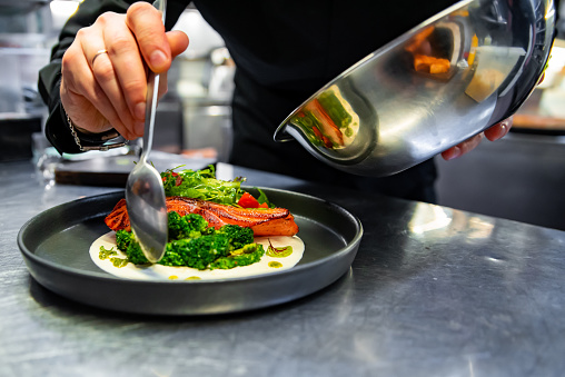 chef hand preparing a gourmet salmon steak with broccoli on restaurant kitchen