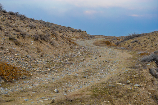 Curved dirty ascending road covered by rocks in a treeless steppe