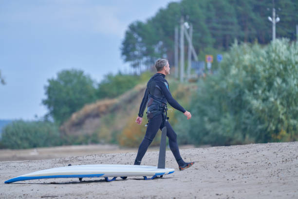 istock Mature man in a wetsuit walks along the shore 1456210828