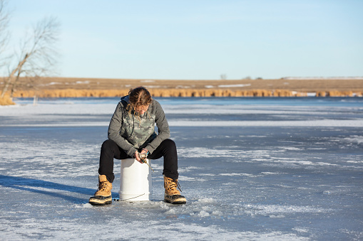 Girl sitting on a five gallon bucket while ice fishing. She is waiting patiently for a fish to bite.