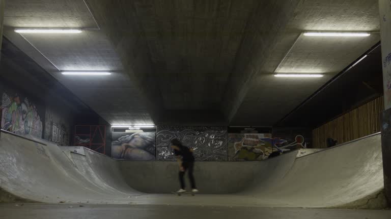 Teenager riding skateboard on underground skatepark ramp, wide shot