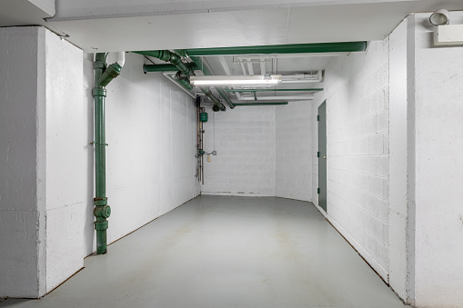 An empty parking garage spot with white walls, green pipes, and concrete floor.