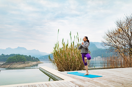 Young adult woman practicing yoga near swimming pool at tourist resort