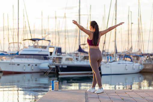Shot of a fitness young woman stretching and preparing for training by the marina with yachts. Active and healthy living concepts.