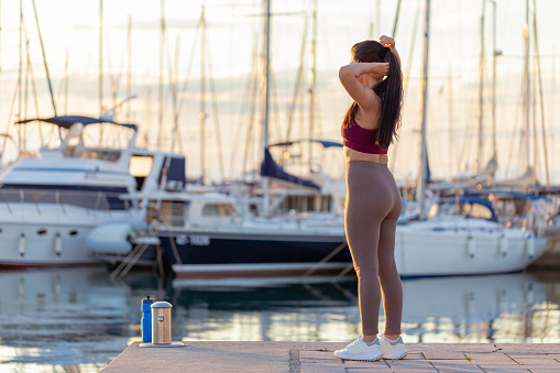 Shot of a fitness young woman fixing her hair for training and standing in the marina.