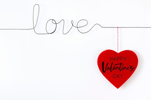 Valentine’s day concept with red felt heart and wire which is shaped as text “love” on white background