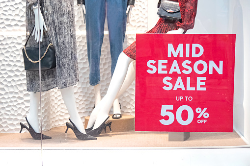 Close-up shot of red mid-season sale up to 50% stickers on retail store window with a background of many female mannequins in fashionable outfit