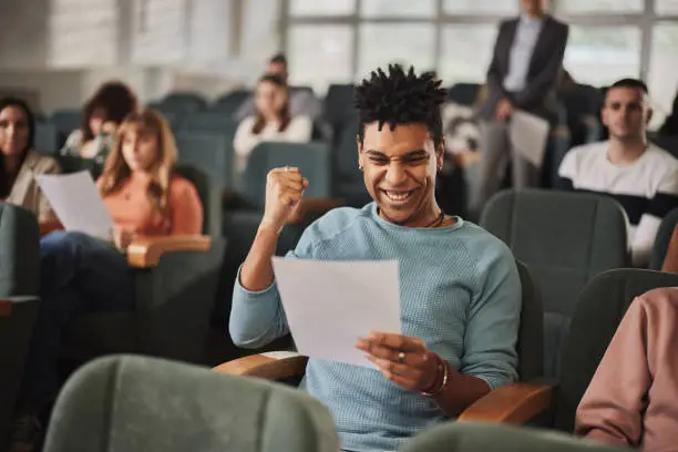 Cheerful African American college student celebrating good test results on a class in amphitheater.