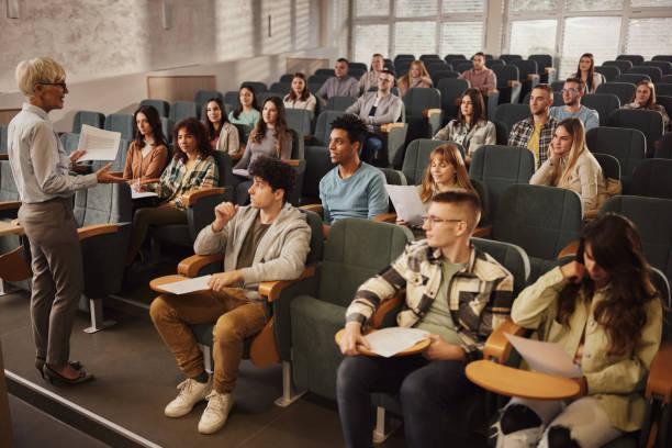 college-studenten hören ihrem leitenden lehrer in einer klasse im hörsaal zu. - hörsaal stock-fotos und bilder