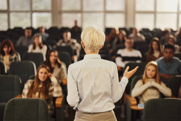 Back view of a female professor teaching her students at lecture hall.