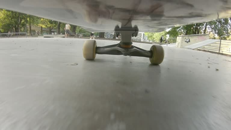 Riding fast on ramp in skatepark, under skateboard close up pov