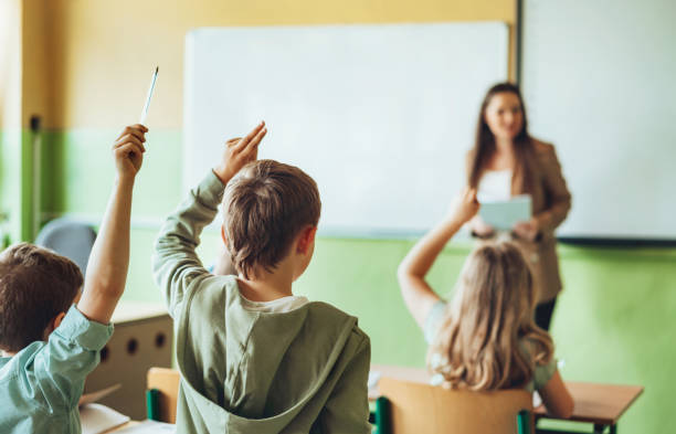 istock Elementary school children in classroom putting up hands for asking questions 1456222322