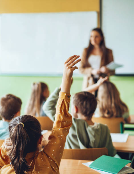 school girl in classroom putting up hands for asking questions - elementary school building imagens e fotografias de stock