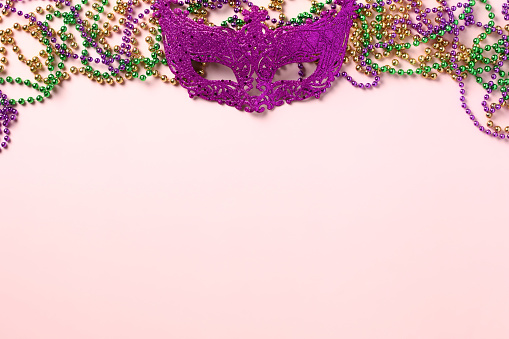 Mardi Gras party invitation card concept. Carnival mask with colorful beads on pink background.