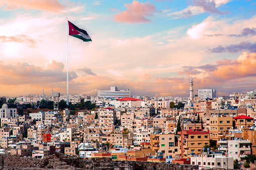 Jordan flag in Amman, cloudy sky background with human houses urban