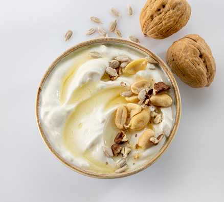 bowl of greek yogurt with honey syrup and nuts on white background, top view