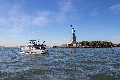 Liberty Island, NY, United States - October 6, 2022: A pleasure boat passing by the Statue of Liberty in New York City Harbour. The statue is a popular tourist destination and a high light for many boaters doing America’s Great Loop.