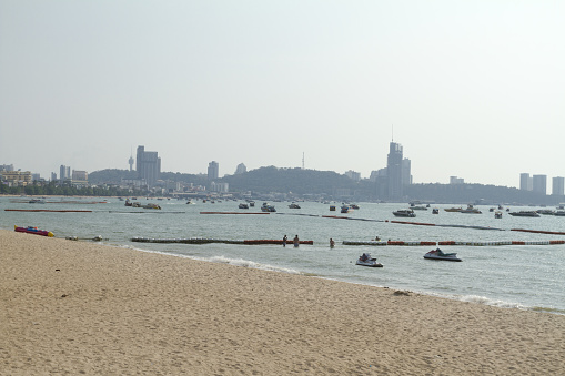 Many anchored boats in Pattaya in sea in front of harbor and beach in Pattaya north. In background is hill with Pattaya south and harbor