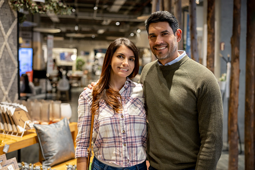 Portrait of a happy Latin American couple shopping at a furniture store and looking at the camera smiling - lifestyle concepts