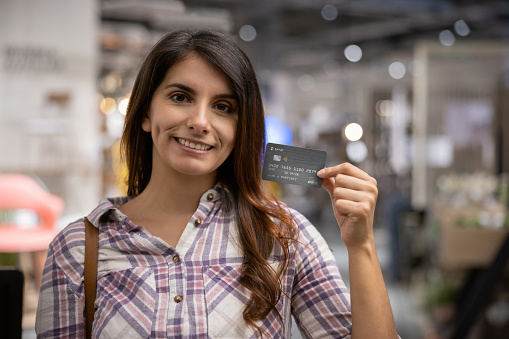 Portrait of a Latin American woman shopping at a furniture store using her credit card and looking at a camera smiling