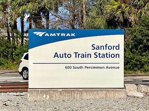 Sanford, Florida, USA - January 8, 2023: A car passes behind the Sanford Amtrak Auto Train Station sign on a sunny afternoon.