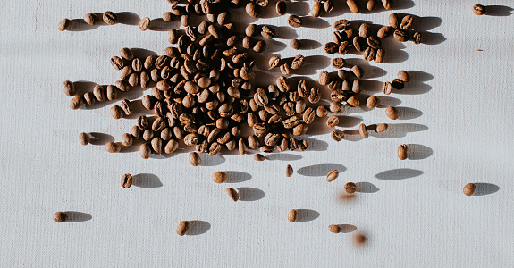 A multitude of whole coffee beans on a white surface, casting shadows. Conceptual with space for copy.
