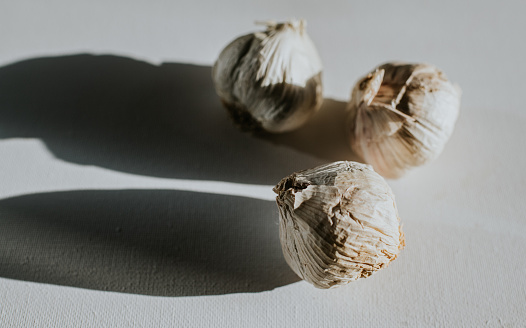Three bulbs of whole, unpeeled garlic on a white surface, casting harsh, long shadows. With space for copy.