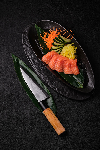 Chefs knife and served salmon sashimi  on black concrete background