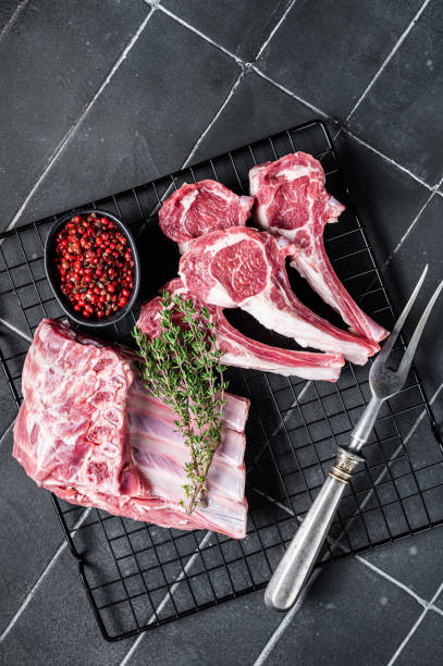 viande d’agneau crue fraîche hacher des steaks sur la table de la cuisine avec des épices et des herbes. fond noir. vue de dessus - rack of lamb chop raw meat photos et images de collection
