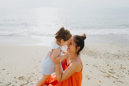 Photo of a young mother with her baby girl, being playful, enjoy each other's company and long walks by the ocean