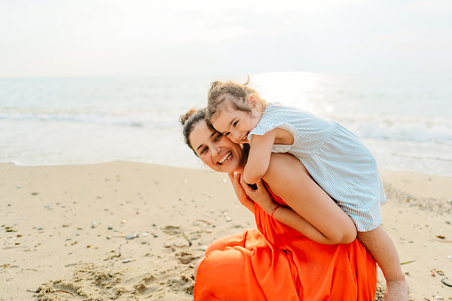 Photo of a young mother with her baby girl, being playful, enjoy each other's company and long walks by the ocean