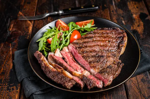 Barbecue grilled and sliced wagyu Rib Eye beef meat steak on a plate. Dark background. Top view.
