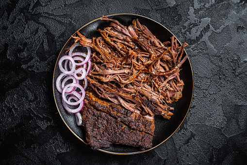 BBQ pulled pork meat on plate. Black background. Top view.