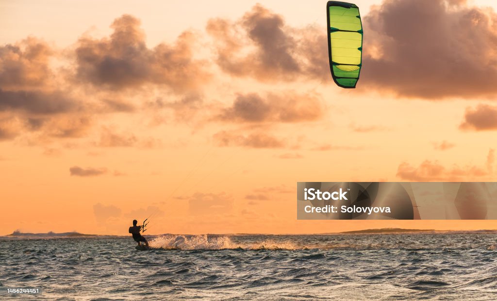 Sunset sky over the Indian Ocean bay with a kiteboarder riding kiteboard with a green bright power kite. Active sport people and beauty in Nature concept image. Le Morne beach, Mauritius. Kiteboarding Stock Photo