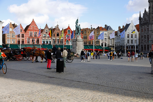 Bruges, Belgium - September 8, 2022: Colorful brick houses form the frontage of Market Square. There is also large bronze statue in the square.