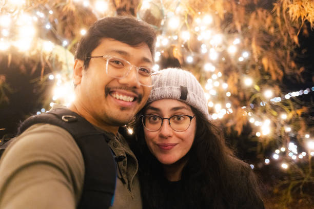 istock Christmas Lights at a Park - Couple Selfie Under a String Light Tree 1456246090